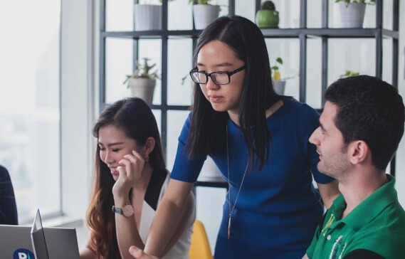 Woman standing over man and woman at working helping on laptop