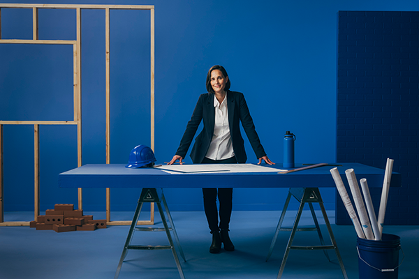 Woman standing behind desk with plans laid across desk.